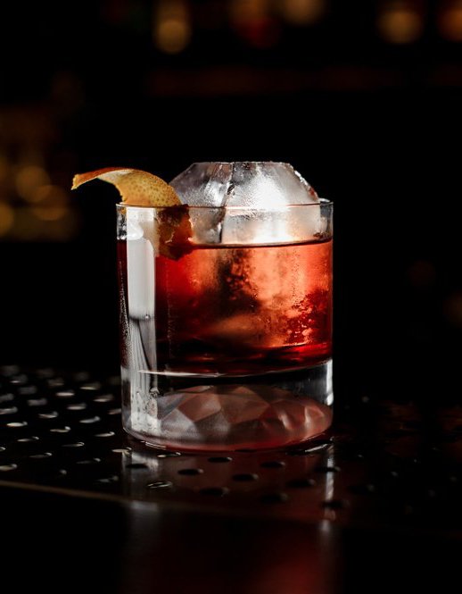Close-up of a red craft cocktail served on the rocks with a citrus twist garnish.