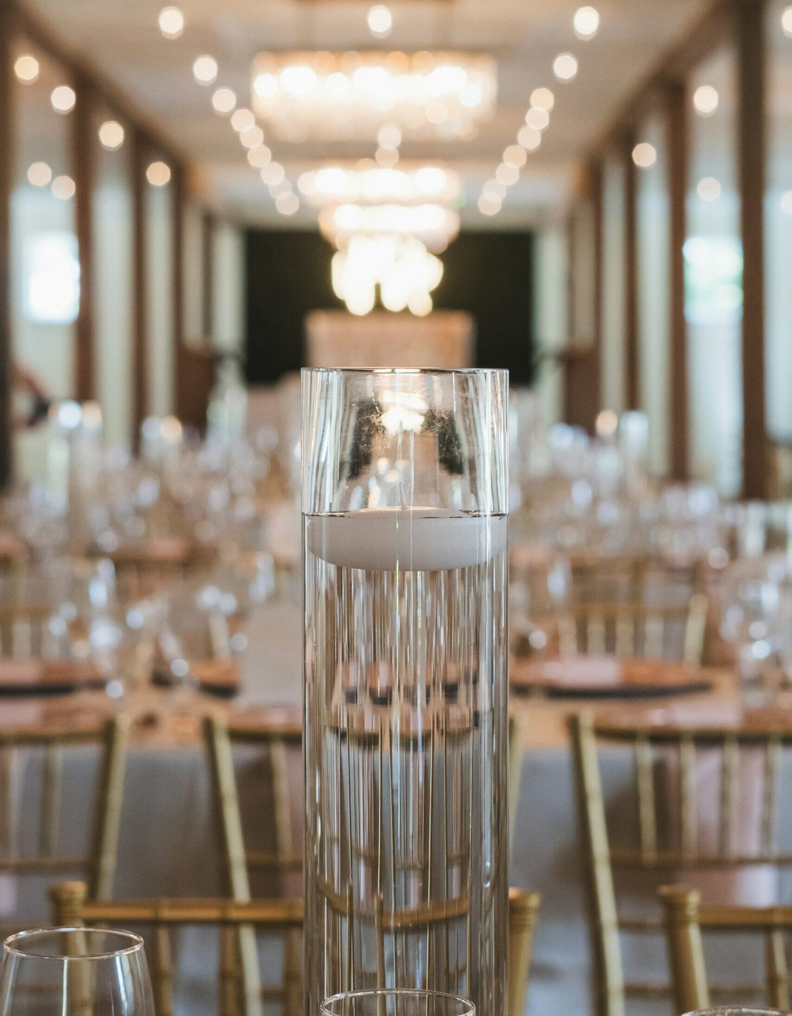 Tall cylindrical glass centerpiece with a floating candle in an elegant wedding reception hall.