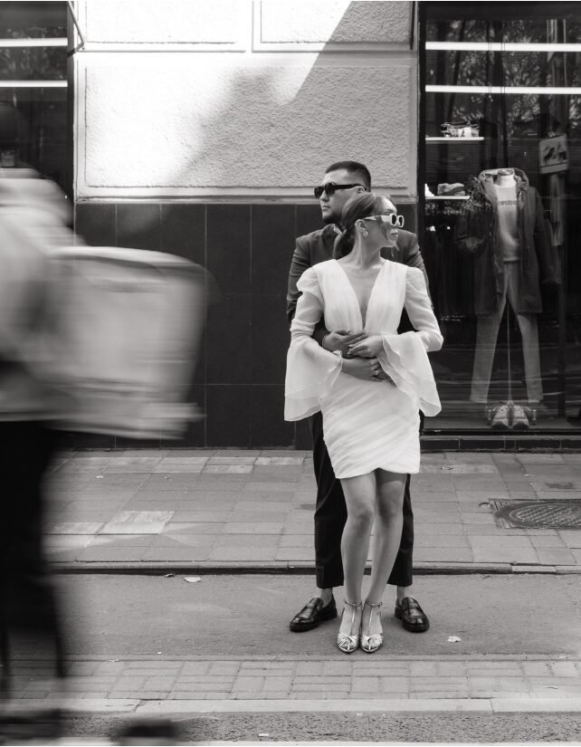Bride and groom in a black-and-white urban wedding photo, capturing a romantic moment on a busy city street.