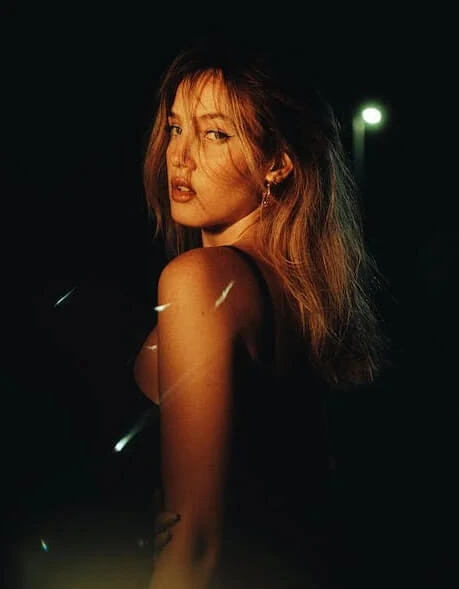 Moody nighttime portrait of a young woman with dramatic lighting highlighting her face and hair.
