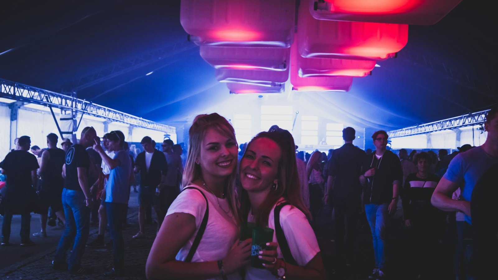 Luxury Party Package | Capturing Gala & Corporate Events by Wave Studio Two smiling women under vibrant pink and blue lighting at a large-scale event or party.