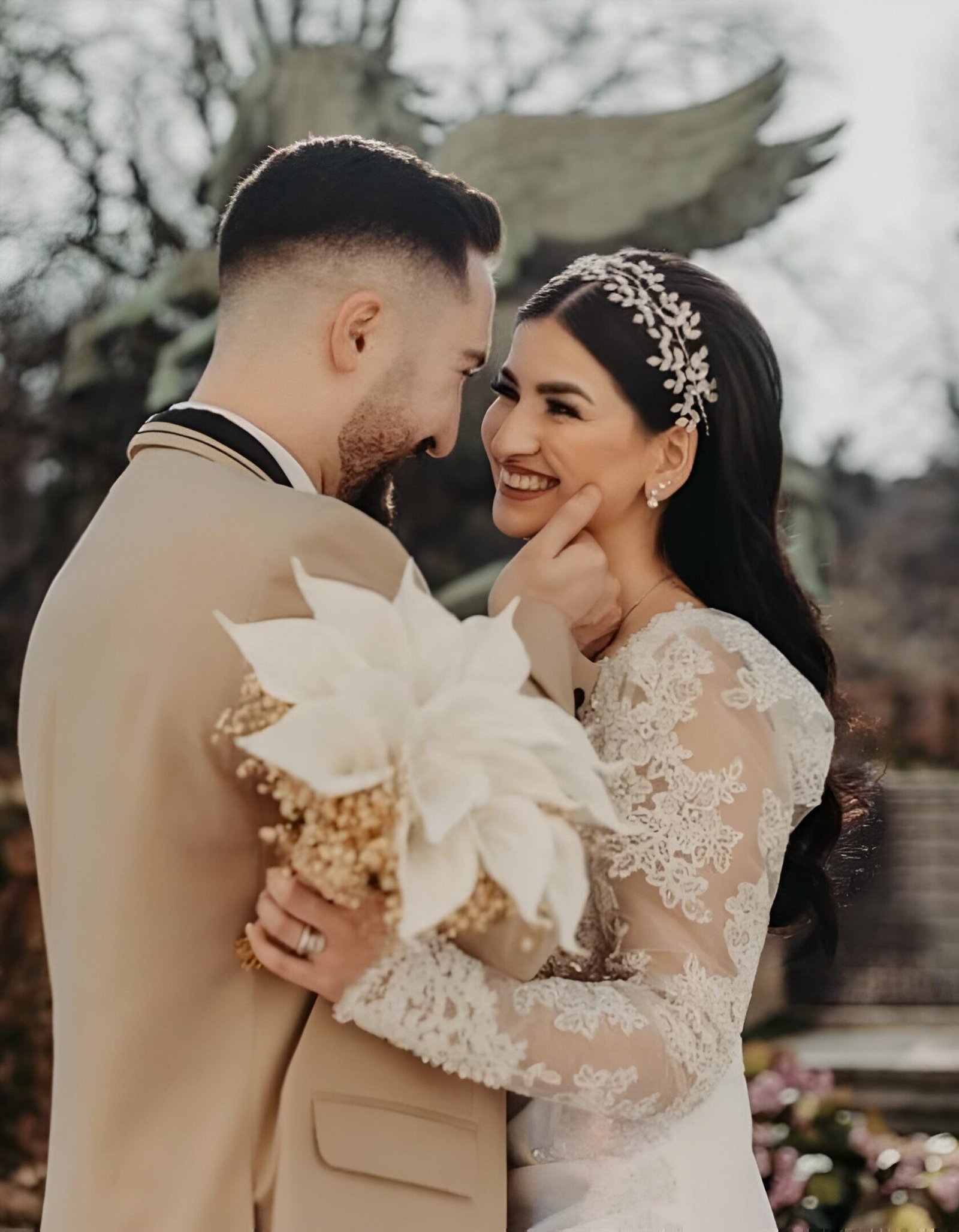 Bride and groom sharing a loving embrace outdoors, with the bride holding a white bouquet and wearing a lace gown.
